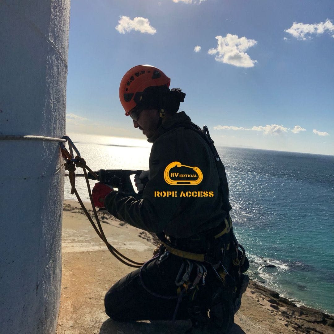 Técnico de 8Vertical instalando un punto de anclaje en lo alto de un faro, con el océano al fondo