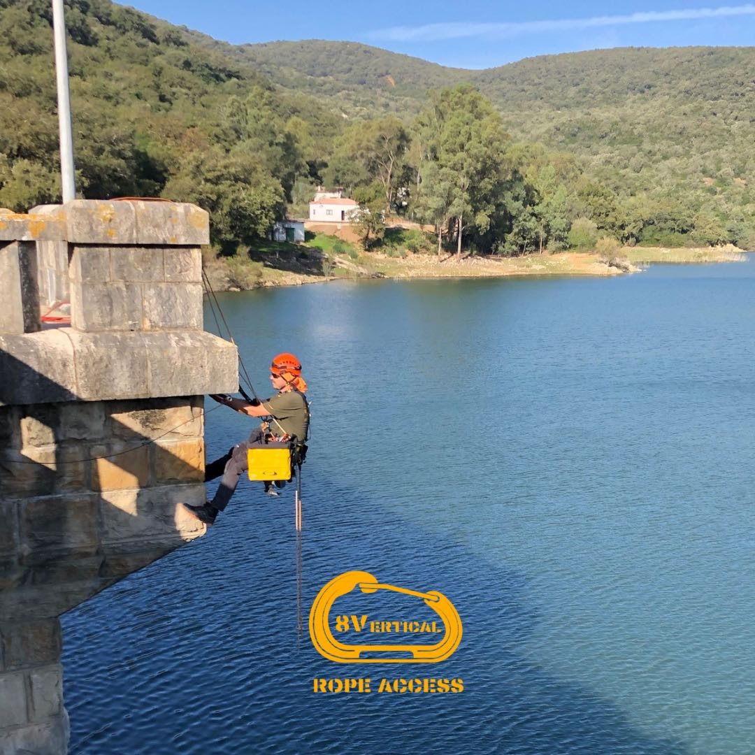 Técnico de 8Vertical descendiendo por un muro de presa junto a un embalse